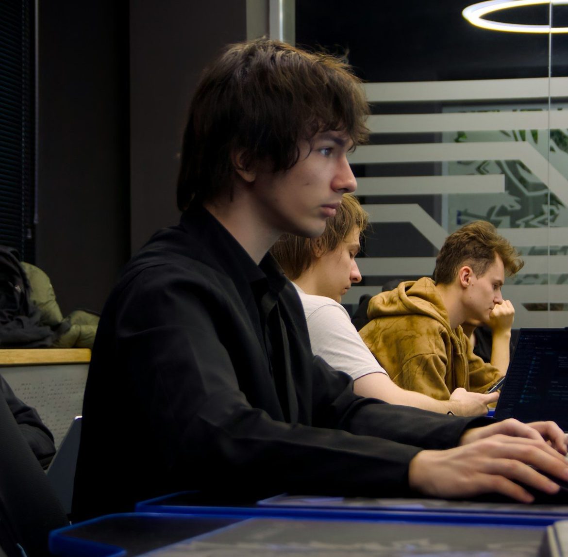 Young man typing on a laptop in a classroom.